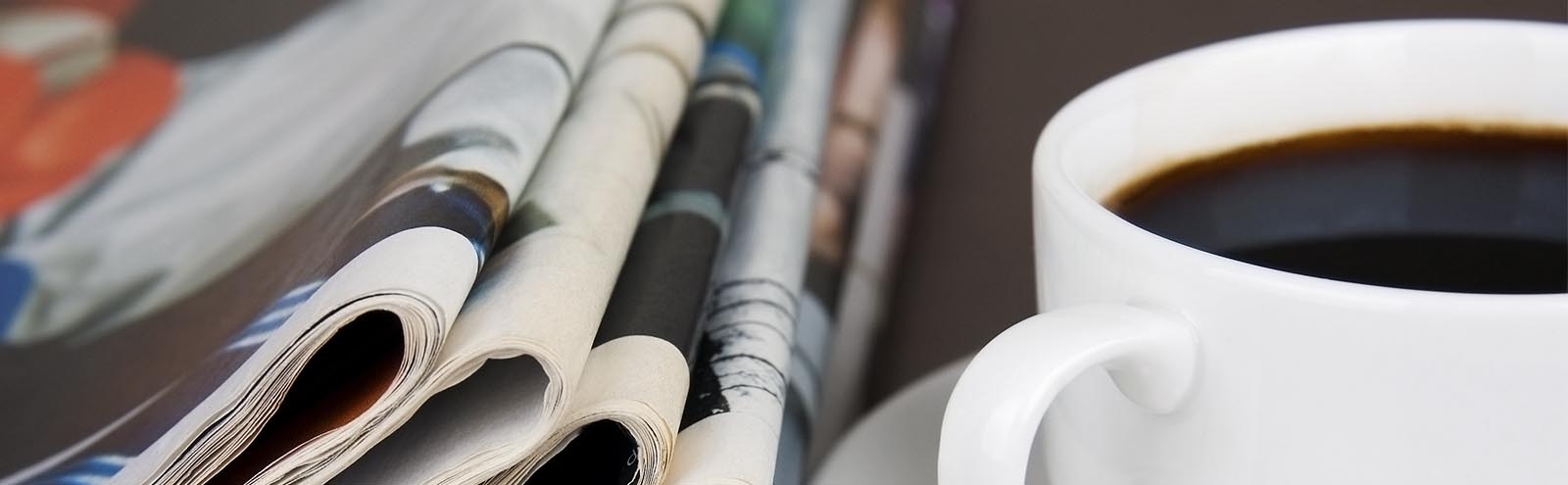 A close up of folded newspapers with a cup of coffee to the right.
