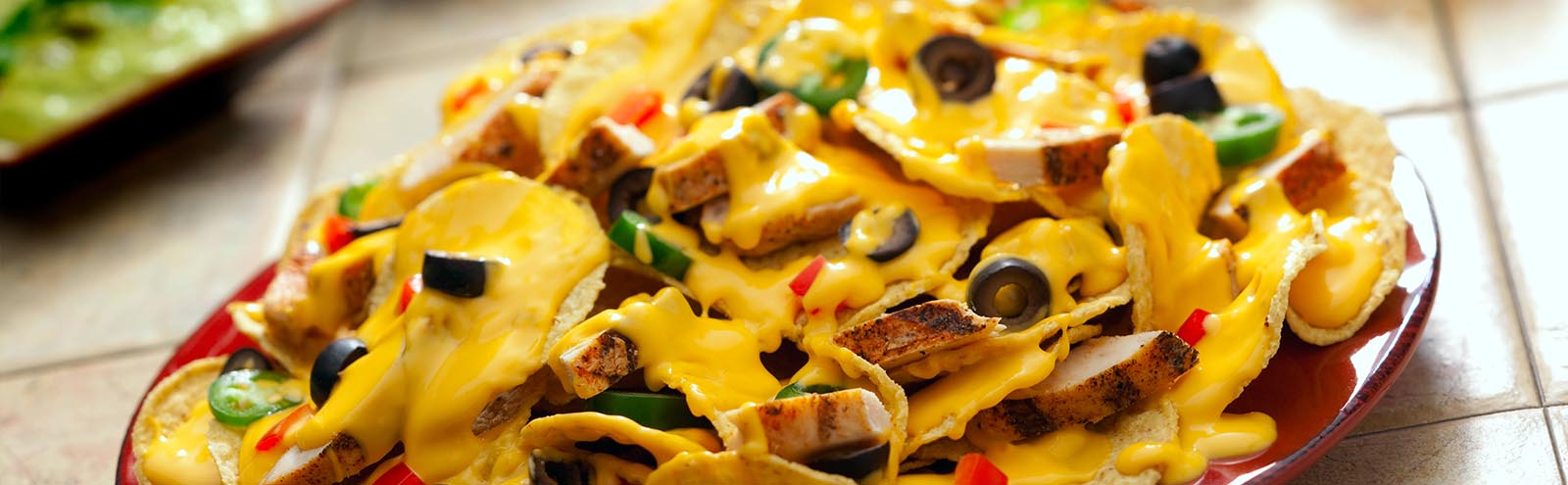 A bowl of nachos with cheese, chicken and olives